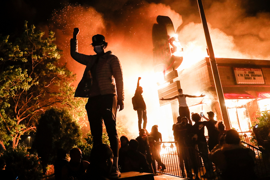 Protesters raise their fists in defiance outside a burning fast food restaurant near the Minneapolis Police Department 3rd Precinct, Friday, May 29, 2020, in Minneapolis. (AP Photo/John Minchillo)